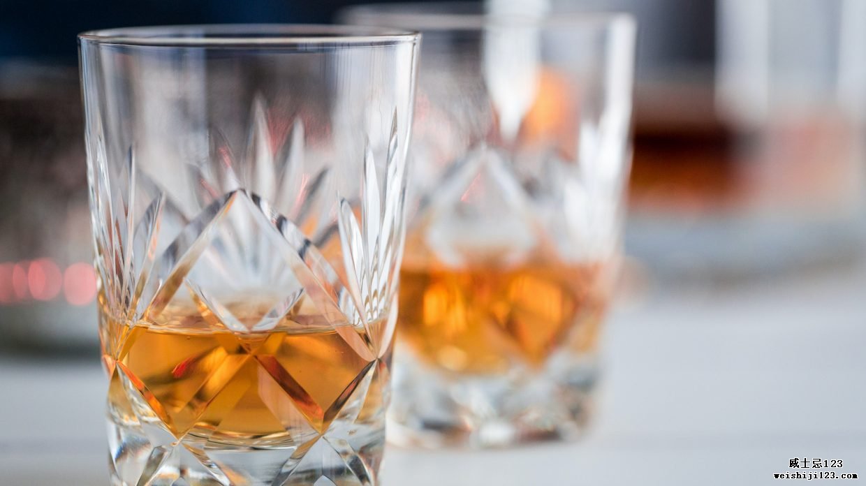 特写彩色图像，描绘了白色木质表面上的两杯精美水晶麦芽威士忌。 威士忌酒杯周围环绕着威士忌用具，例如玻璃醒酒器和酒壶。 复制空间的空间。