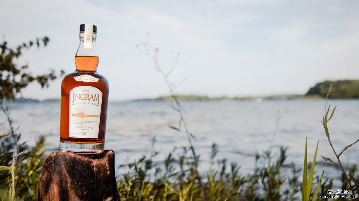 一瓶 OH Ingram River Aged 纯威士忌放在植被中的木桩上，背景中似乎是一条河流。