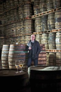 爱尔兰酿酒有限公司的成熟主管凯文·奥戈曼 (Kevin O'Gorman) 靠在一个大桶上，手里拿着一杯威士忌。