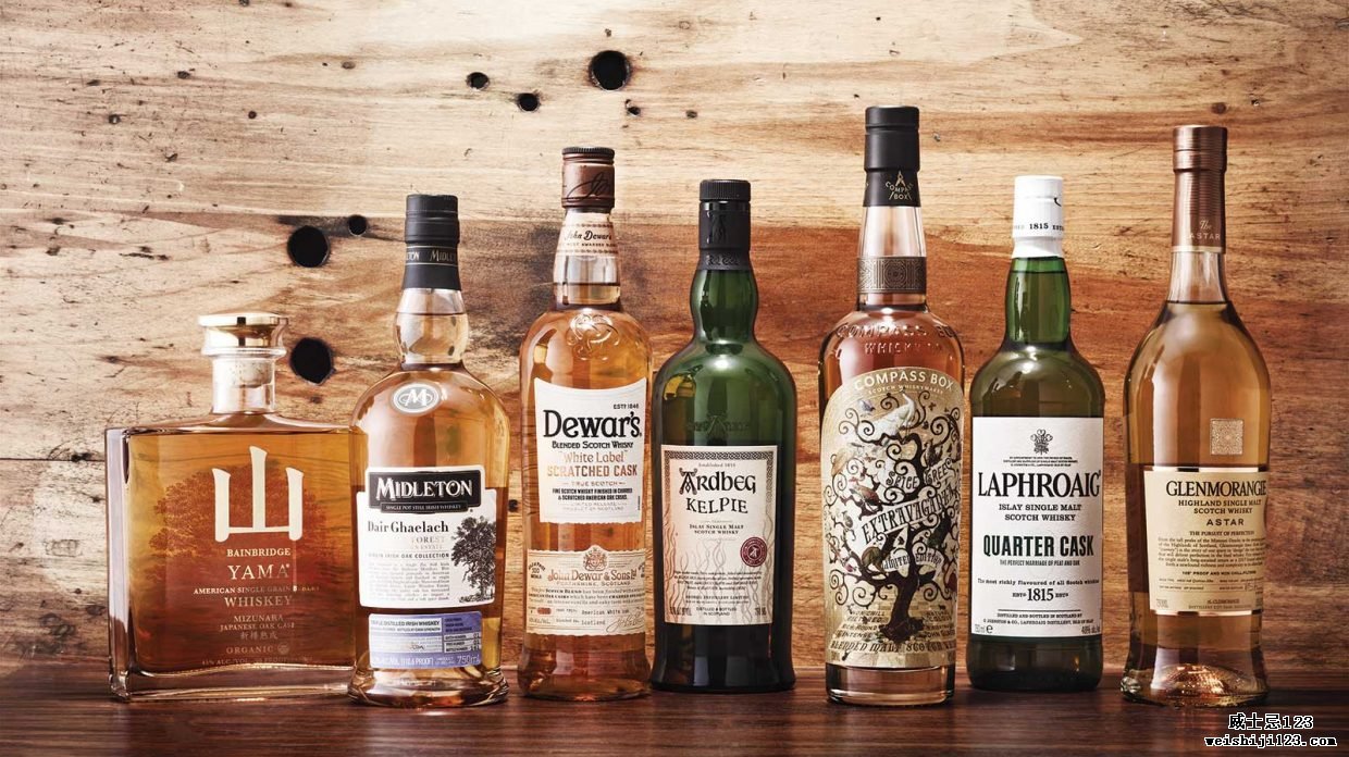 几瓶在定制酒桶中成熟的威士忌放在木墙前的木质表面上。