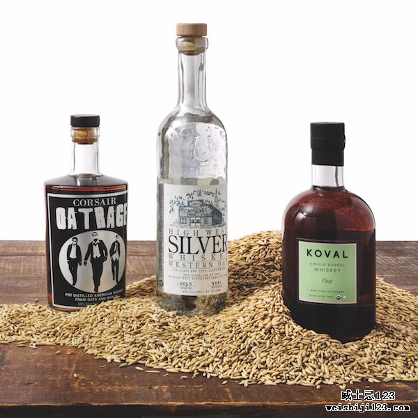 三种不同的燕麦威士忌——Corsair Oatrage、High West Silver Western Oat 和 Koval Single Barrel Oat——放在木质表面上，燕麦散落在它们面前。