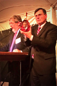 DISCUS 总裁兼首席执行官 Adm. Peter Cressy 在 2014 年 10 月 14 日弗农山烈酒拍卖会上拿着比尔·克林顿签名的一瓶乔治·华盛顿的黑麦。照片由 DISCUS 提供。